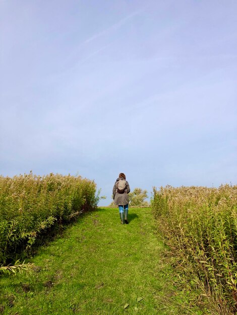 Rear view of woman climbing a grassy hill under a lightly clouded sky