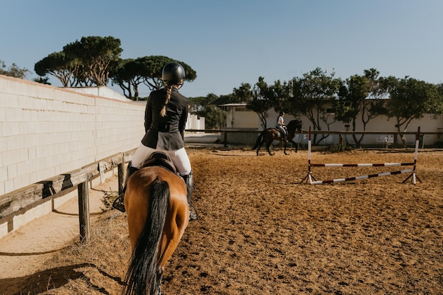 Rear view of a woman in equestrian attire warming up a horse by circling the equestrian arena