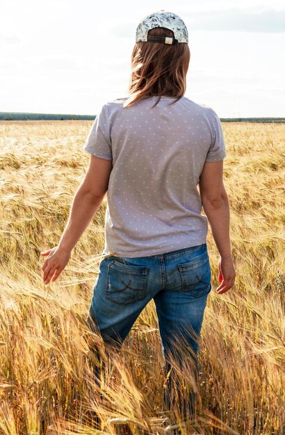 Rear view woman in jeans among yellow dry cereal wheat field agriculture and grain harvest Mockup