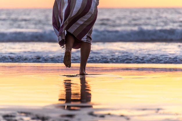 Photo rear view of woman legs walking on a beach to the ocean at sunset time.copy space