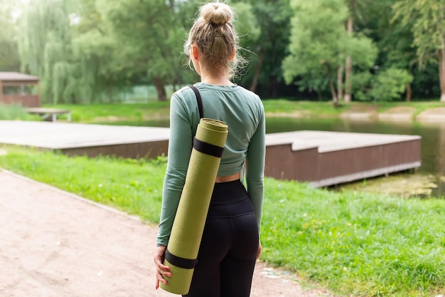 Rear view a woman in the park in summer with a green gym mat behind her back