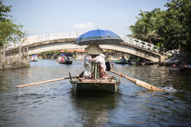 Rear view of woman rowing boat in river against bridge