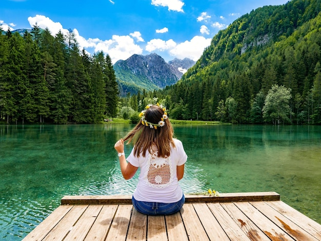 Photo rear view of woman sitting on pier at lake against mountains