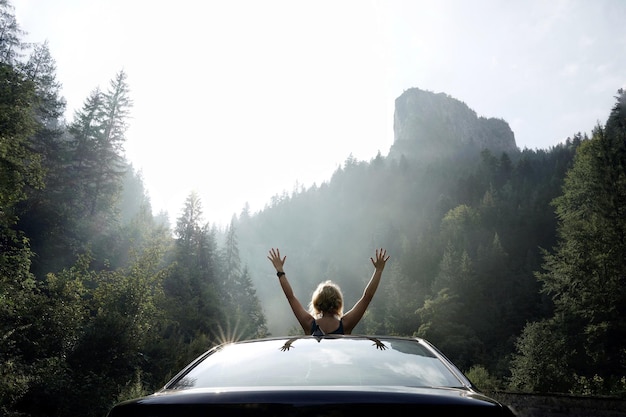 Photo rear view of woman with arms raised in car at forest against sky