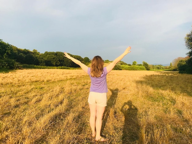 Photo rear view of woman with arms raised standing on field against sky