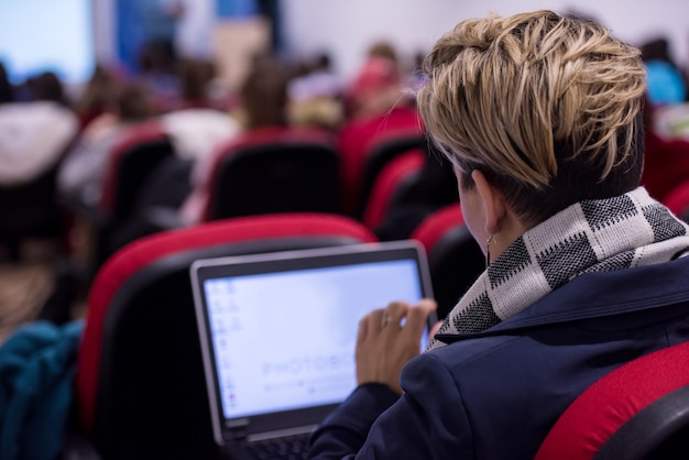 rear view of young businesswoman typing on laptop computer keyboard during the seminar at conference room