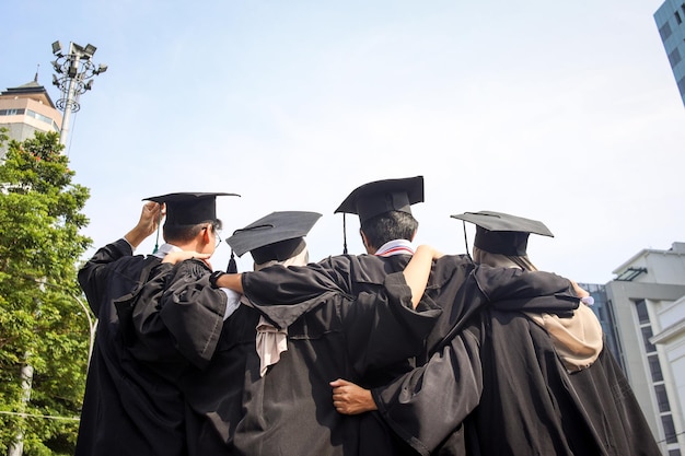 Rear view of young group of happy multiracial graduate friends hugging each other standing in a row