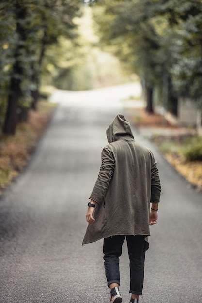 Rear view of a young male in a jacket with a hood walking in the empty street