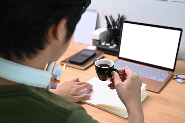 Rear view young man drinking coffee and working from home with laptop computer