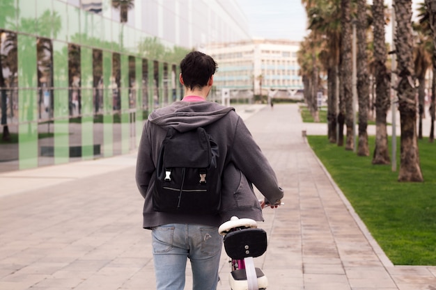 Rear view of a young man walking pushing a bike