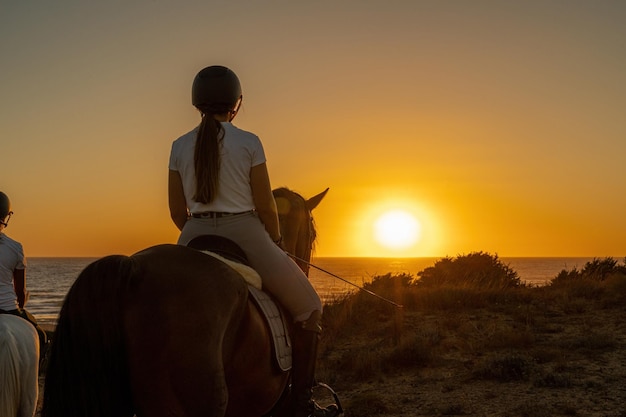 Rear view of young woman on horseback watching the sunset