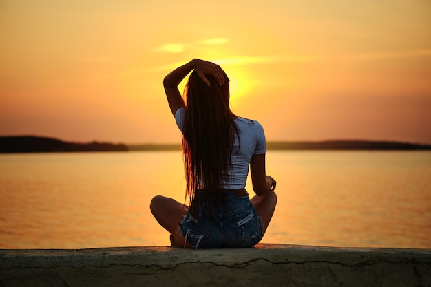 Rear view of young woman sitting on a pier during the sunset