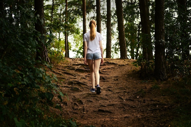 Rear view of a young woman walks along a forest path