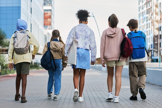 Rear view of youthful interracial pupils walking down street