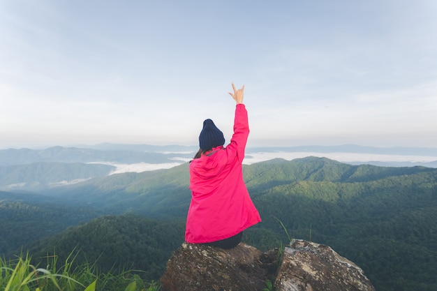 Rear of young woman sitting on rock and see view on top mountain