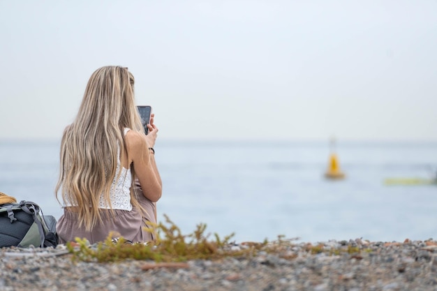 Rearview of woman with blonde hair is looking her smartphone in a cloudy day