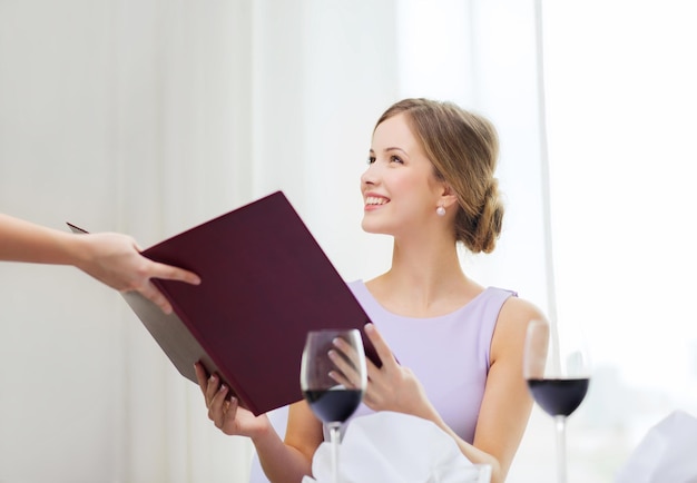 reastaurant and happiness concept - smiling young woman recieving menu from waiter at restaurant