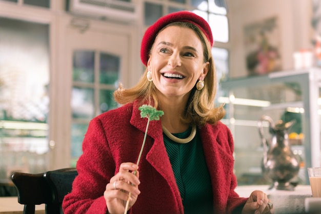 Receiving flower. Happy beaming mature woman wearing red beret feeling amazing after receiving flower