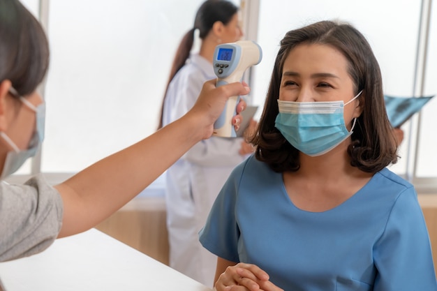 Receptionist and guest wearing face mask at front desk while having conversation in office or hospital