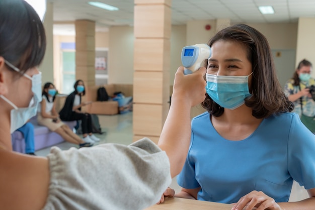 Receptionist and guest wearing face mask at front desk while having conversation in office or hospital