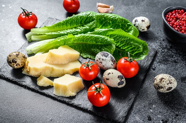 Recipe for Caesar salad, Romaine lettuce, tomatoes, eggs, Parmesan, garlic, pepper. Black background. Top view.