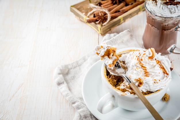 Recipes with pumpkins, fast food, microwave meal. Spicy pumpkin pie in mug, with whipped cream, ice cream, cinnamon, anise. On white wooden table, with cup of hot chocolate. 