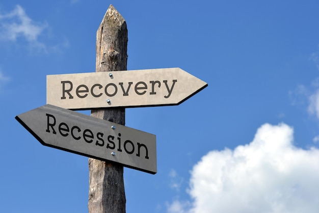 Recovery or recession wooden signpost with two arrows sky with clouds