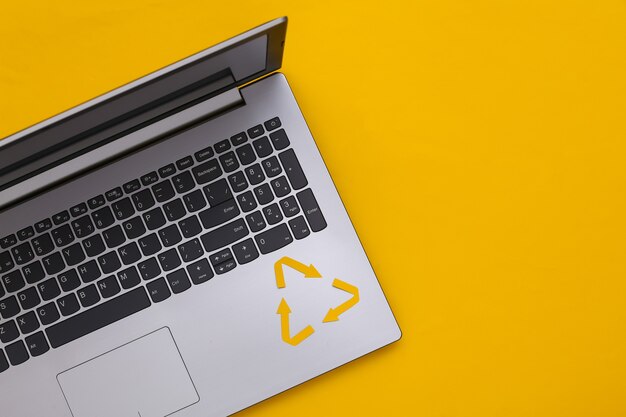 Recycled arrows sign and laptop keyboard on yellow background. Top view