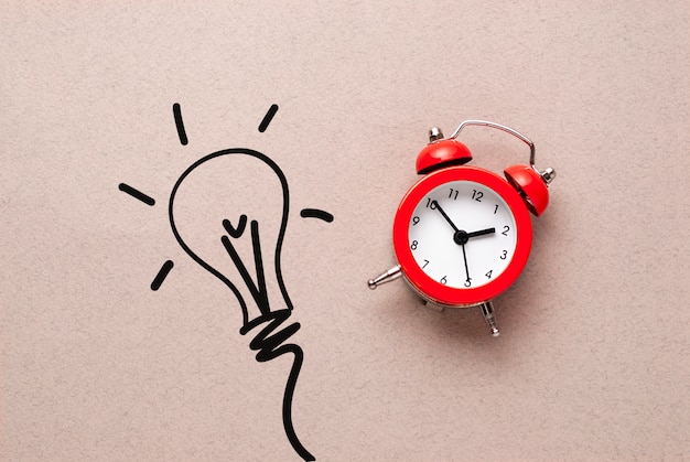 Red alarm clock alongside a sketch of a light bulb