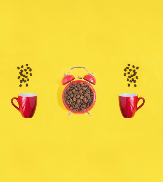 Red alarm clock and coffee cups with coffee beads on the yellow background Top view Copy space