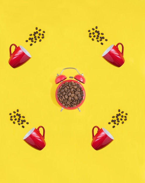 Red alarm clock and coffee cups with coffee beads on the yellow background Top view Copy space