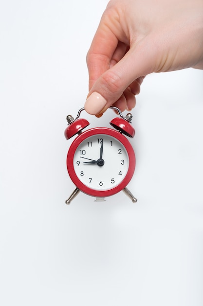 Red alarm clock in a female hand on a white surface