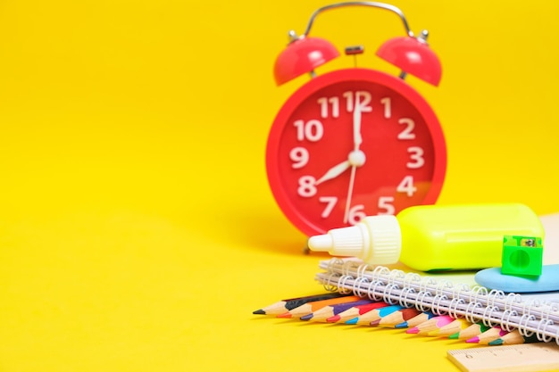 Red alarm clock and school supplies yellow backgroundPreparing child for school