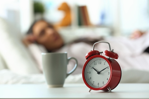 Red alarm clock at ten oclock and sleeping woman