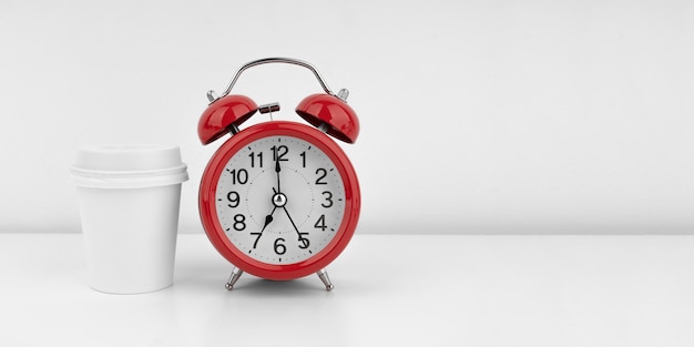 Red alarm clock with cofeecup on white wall background