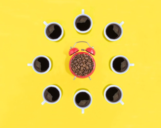 Photo red alarm clock with coffee beads and coffee cups on the yellow background top view copy space