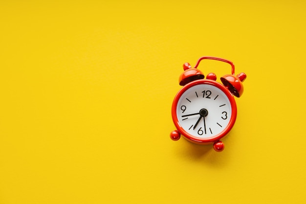 Red alarm clock on a yellow paper background Minimalistic image