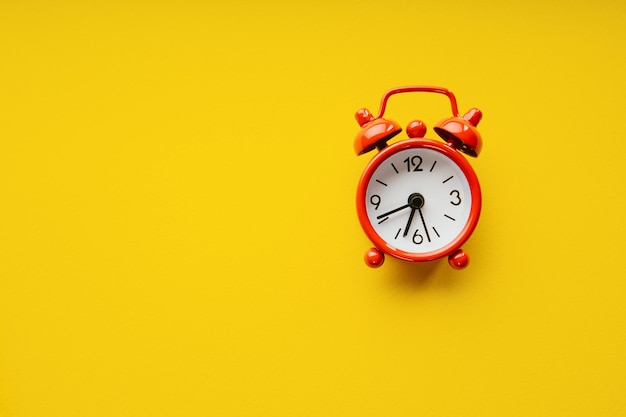 Red alarm clock on a yellow paper background