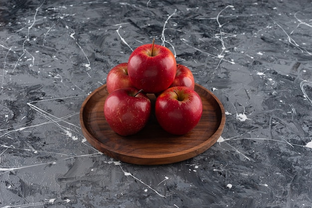 Red apple fruits placed on a round wooden plate.