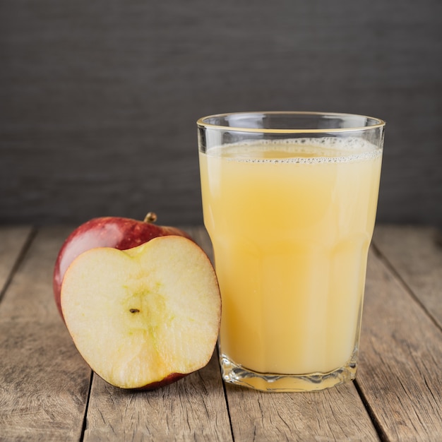 Red apple juice in a glass with fruits over wooden table