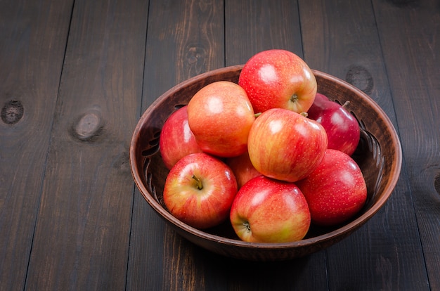 Red apples on a dark rustic background in a clay bowl.  Flat lay.