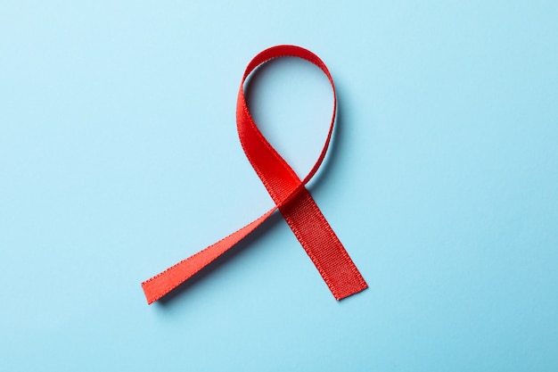 Red awareness ribbon on blue background, close up