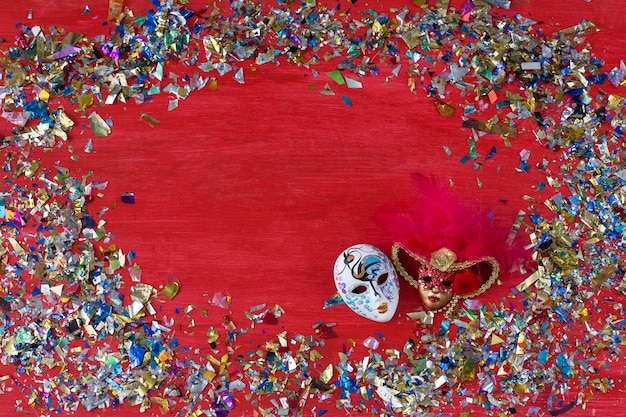 On a red background are two carnival masks and colored confetti around