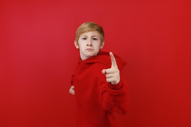 On a red background a boy dressed in a red tracksuit shows threatening signs