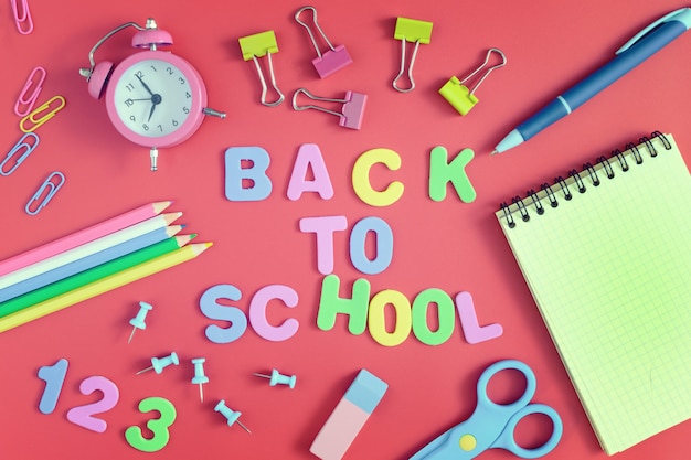 On a red background, there are paperclips, a notebook, an alarm clock and school supplies. 