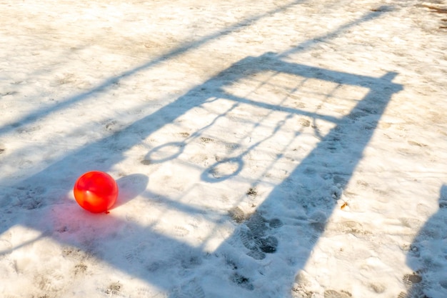 Red ball in the snow on the background of the shadow of the rings