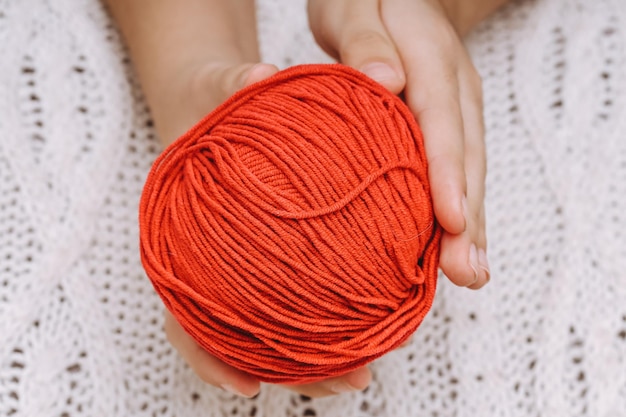 Red ball of wool in hands on the background of a white knitted tablecloth. High quality photo