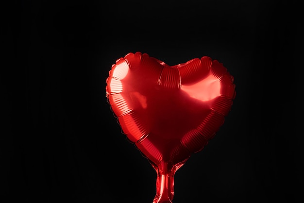 Red balloon in the shape of a heart on black background selective focus