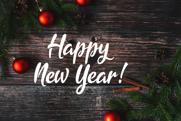 Red balls with fir branches on a wooden background and the inscription Happy New Year