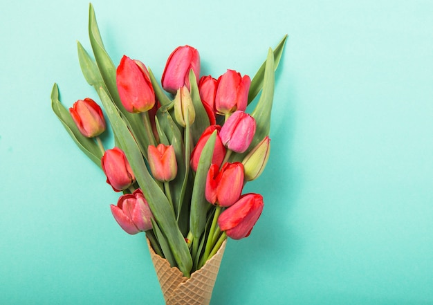 Photo red  beautiful tulips in an ice cream waffle cone on a color blue background. conceptual idea of a flower gift. spring mood